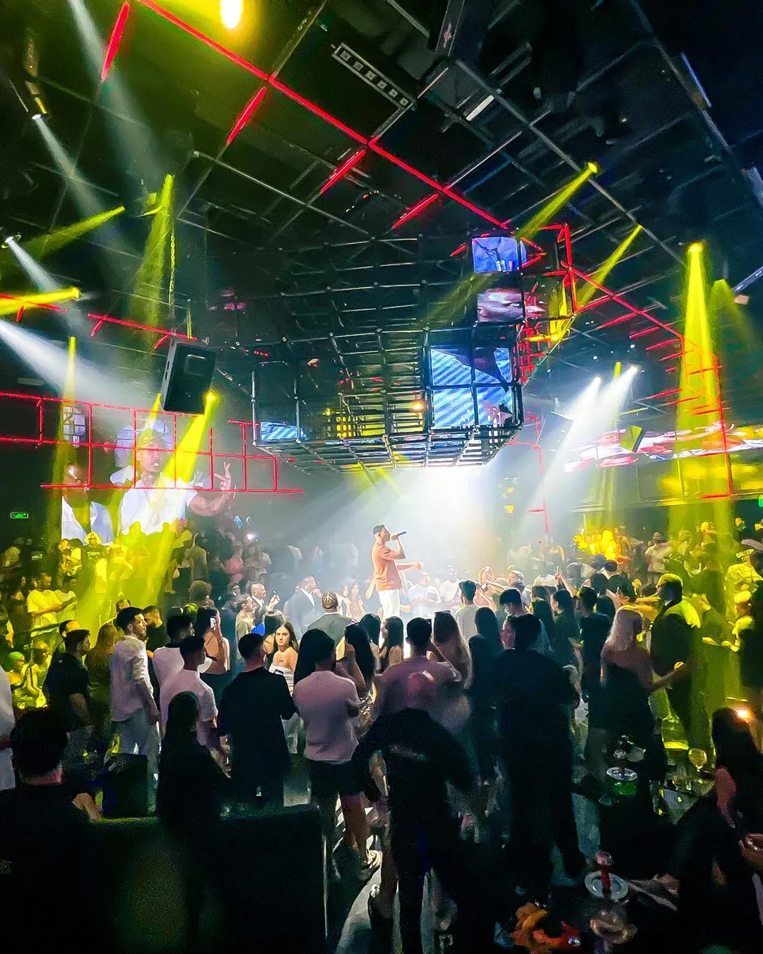 Singer performing on stage as the crowd dances under yellow spotlights